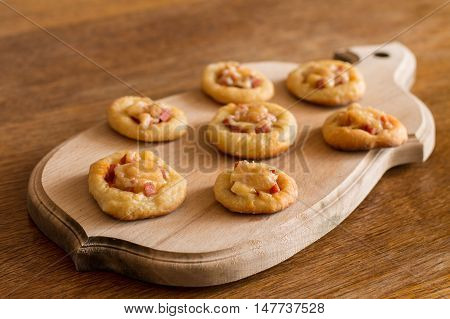 Mini pizzas with sausage and cheese on cutting board on wood table.