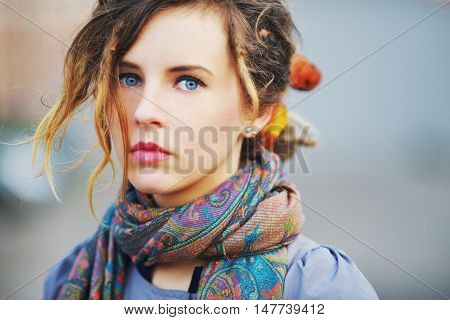 Gorgeous portrait of a young serious girl with beautiful blue eyes and youthful hair in the scarf with a color picture closeup.