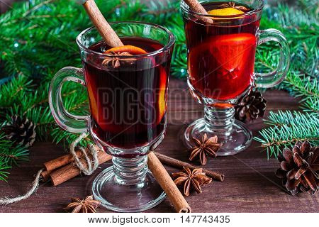 two glasses of hot christmas mulled wine with christmas tree pine cones on wooden background