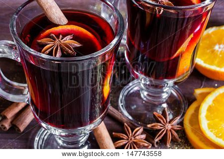two glasses of hot mulled wine with spices and sliced orange on wooden background. close up