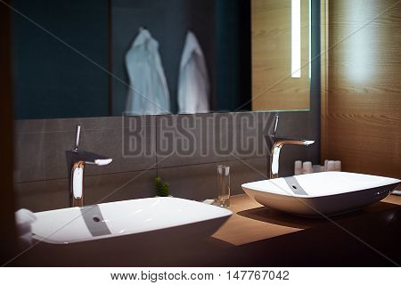 Modern bathroom closeup to a mirror and countertop sink and towels next to liquid soap dressing room can be seen through the door