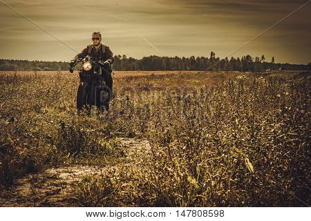 Young, stylish man on the vintage custom racer in a field.