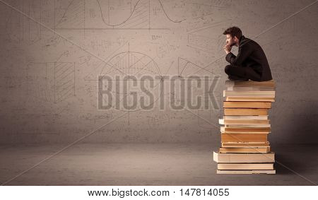 A serious businessman in suit sitting on a pile of giant books in front of a greyish brown wall with drawn lines, angles, numbers, circles and curves.