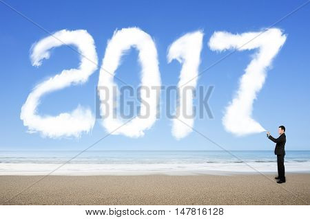 Businessman spraying white 2017 year cloud shape in blue sky on sea beach background.
