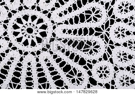 Star and circles in a white crocheted doily. Crochet is a process of creating fabric by interlocking loops of yarn  using a crochet hook. Macro photo close up from above on black background.