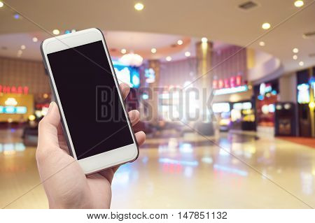 Human Holding Mobile Phone with blank screen on Department store blurred background