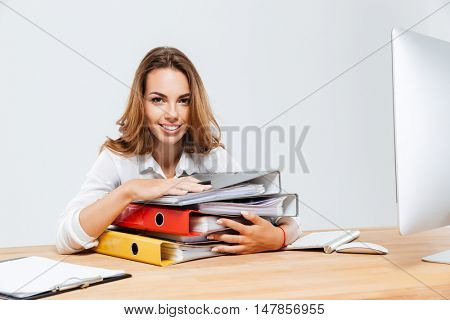 Close up of a happy businesswoman holding folders while sitting at the office desk isoltaed on the white background