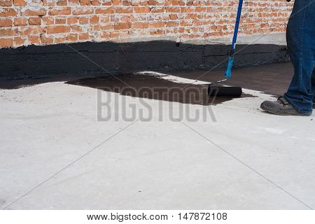 Worker covered surface bitumen primer for improving adhesion during surfacing rolled waterproofing during the installation of isolation on industrial or household objects