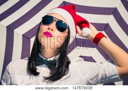 Portrait close up of a pretty young woman in Santa Claus hat and sunglasses with bright painted pink lips next to striped background