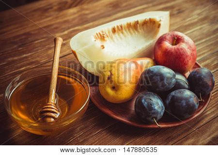 Fresh juicy ripe fruits of the new harvest. Fresh fruits and harvest honey on a brown wooden table. Apples pears plums melon raspberry honey on the table.