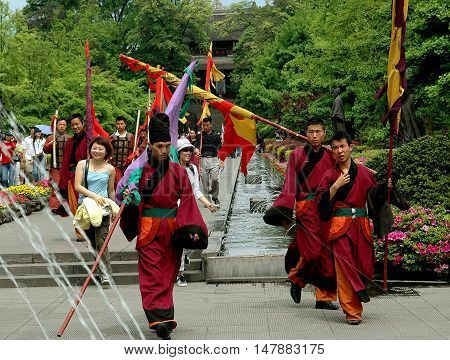Dujiangyan China - April 24 2005: Taoist monks carrying flags walking in the gardens at Dujiangyan Historic Park