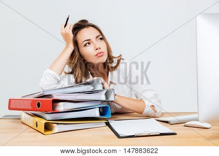 Pensive young businessman sitting at the office desk and holding pen isoltaed on the white background