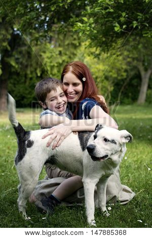 Nice white boy with beautiful young woman on spring sunny garden. Portrait of boy with mother and their dog. Happy family in sunny day. Mother and sun spend leisure time activitie. Playing with dog.