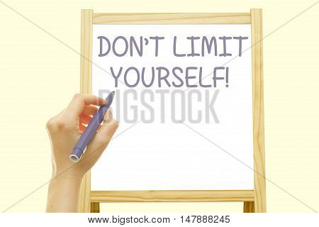 Woman hand writing DON'T LIMIT YOURSELF message on a transparent wipe board.