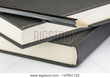 Black wooden pencil to write on two black stacked write notebooks