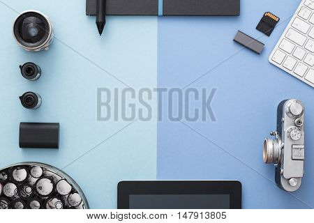 Work space on blue table of a creative designer or photographer with laptop tablet camera and other objects of inspiration and copy space. Stylish home studio concept of technology trends. View from above.