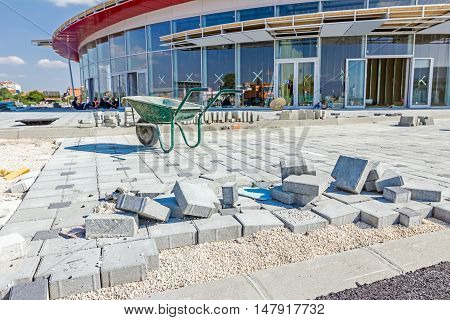 Dirty wheelbarrow is at building site. New pavement is made of cobblestone blocks still under construction.