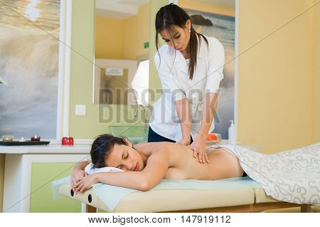 Young woman enjoying back massage in beauty spa salon.