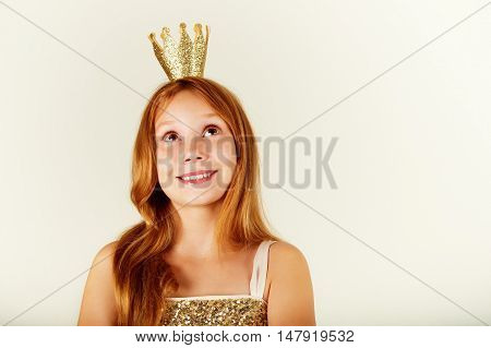 Pretty little girl with beautiful red hair looking up. Little princess with a crown on her head. Kids fashion. toned image