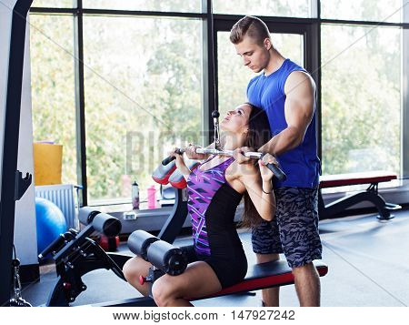 Young athletic woman doing pull down exercise for the back under a personal instructor supervision