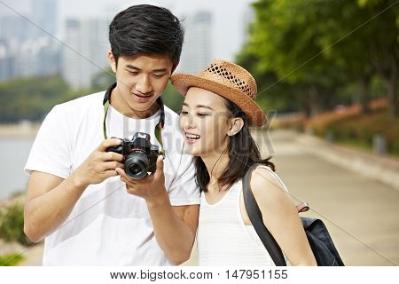 young asian couple tourists looking at camera's monitor checking pictures taken