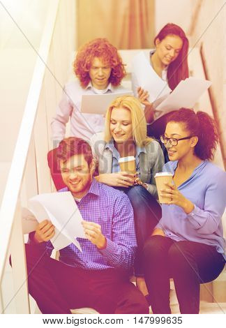 business, office and startup concept - smiling creative team with papers and take away coffee on staircase