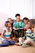 una madre africana feliz leyendo un libro a sus 4 hijos en la sala de estar