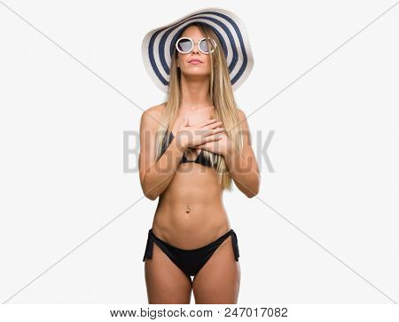 Beautiful young woman wearing bikini, sunglasses and hat smiling with hands on chest with closed eyes and grateful gesture on face. Health concept.