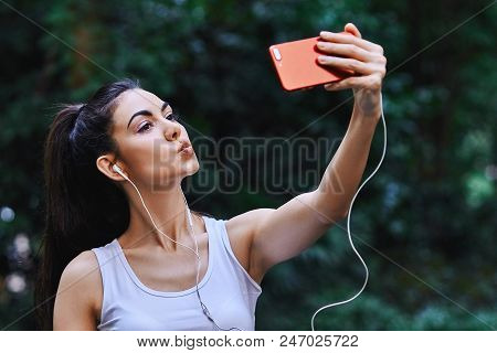 Young Girl Is Taking Picture Of Herself Using Red Cell Phone And Listening To The Music Using White 