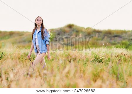 Happy Smiling Young Girl Wearing Blue Jeans Jacket And Shorts Is Standing In The Field