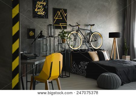 Yellow Chair At Desk With Typewriter In Dark Room Interior With Pouf And Bicycle Near Bed. Real Phot