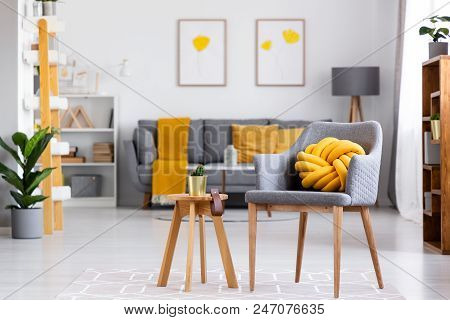 Yellow Knot Cushion On A Gray Armchair Standing Next To A Wooden Stool With A Cactus On It In Cozy L