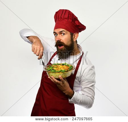 Cook With Happy Face In Burgundy Uniform Holds Baked Dish. Chef Holds Bowl With Potato Casserole And