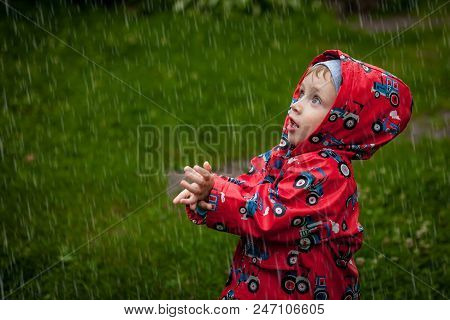 Little Boy In A Waterproof Jacket In Tractors Catch The Rain. Child Having Fun Outdoors In Summer Sh