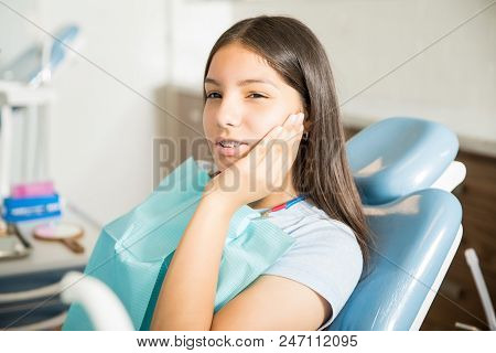 Teenage Girl Suffering From Toothache While Sitting On Chair At Clinic