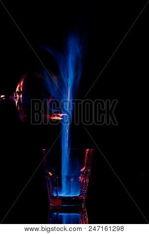 Close Up View Of Pouring Burning Sambuca Alcohol Drink Into Glass Process On Black Background