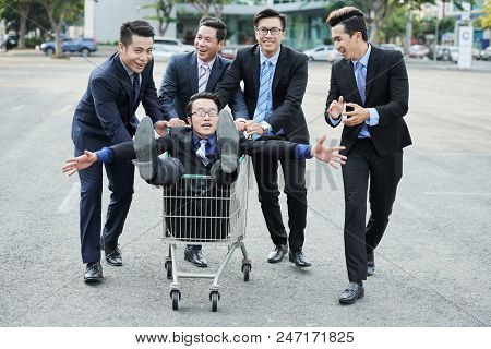 Group Of Cheerul Vietnamse Business People Pushing Shopping Cart With Coworker Sitting Inside