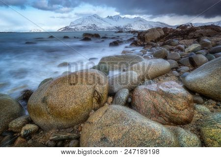 Stones At Beach Of Northern Norway. In Background Snow-capped Peaks Of Cold End Of The World Mountai