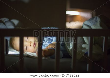 Adorable Newborn Baby Boy, Sleeping In Crib At Night. Little Boy In White Pajamas Taking A Nap In Da