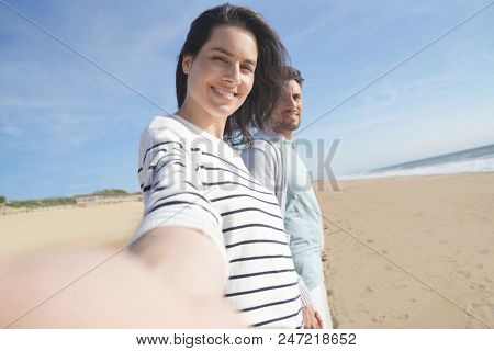 Cheerful brunette woman wallking on the beach, leading camera towards her