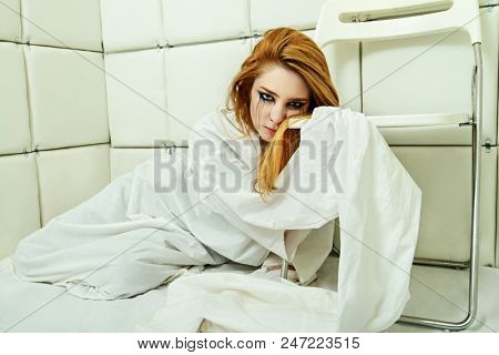 Portrait of a crazy girl dressed in a straitjacket in an isolated room in a madhouse.