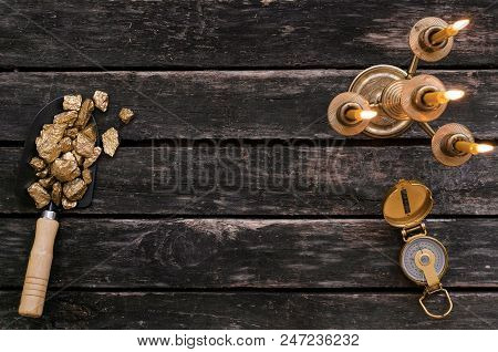 Gold Ore Nuggets In Shovel, Compass And Burning Candle On Old Adventurer Table. Goldminer Treasure H