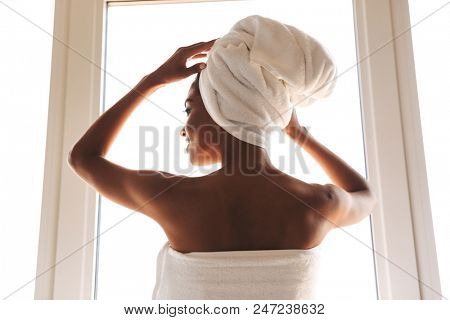 Back view of a sensual african woman wrapped in a towel standing in front of the wondow