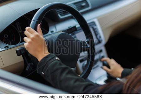 Girls Hands Are Aestetically Situated On The Black Steering Wheel In A Grey Car.