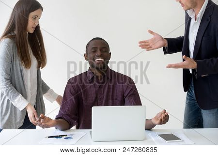 Happy African American Employee Meditating At Desk, Reaching Nirvana State Ignoring Colleagues Talki