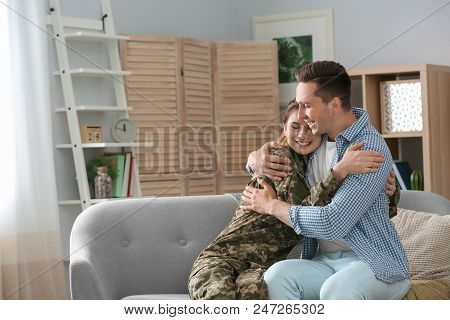 Woman In Military Uniform With Her Husband On Sofa At Home