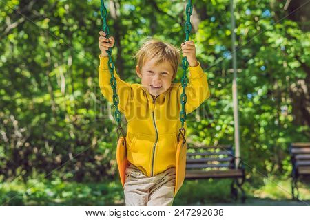 A Boy In A Yellow Sweatshirt Sits On A Swing On A Playground In Autumn.