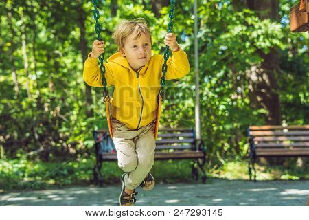 A Boy In A Yellow Sweatshirt Sits On A Swing On A Playground In Autumn.