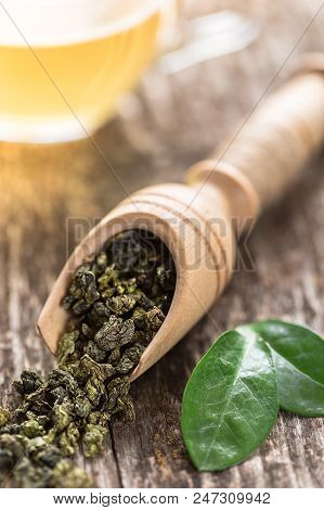 Spoon Of Dried Green Tea Leaves On Wooden Background. Leaves Of Green Tea Close Up