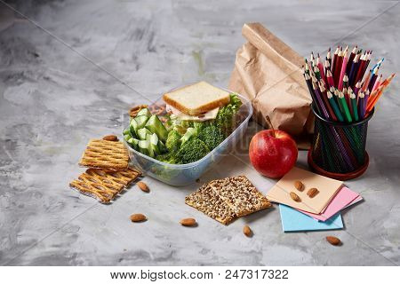 Back To School Concept, School Supplies, Assortment Of Biscuits And Transparent Lunchbox Full Of San